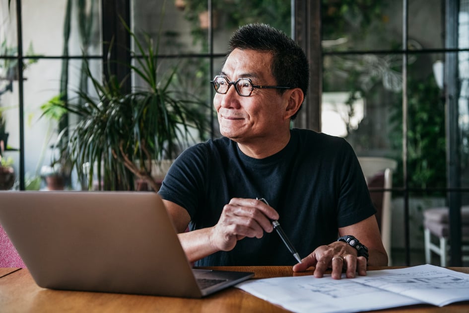 Cheerful man in his 50s sitting at table and looking away, doing paperwork, contemplation, ideas