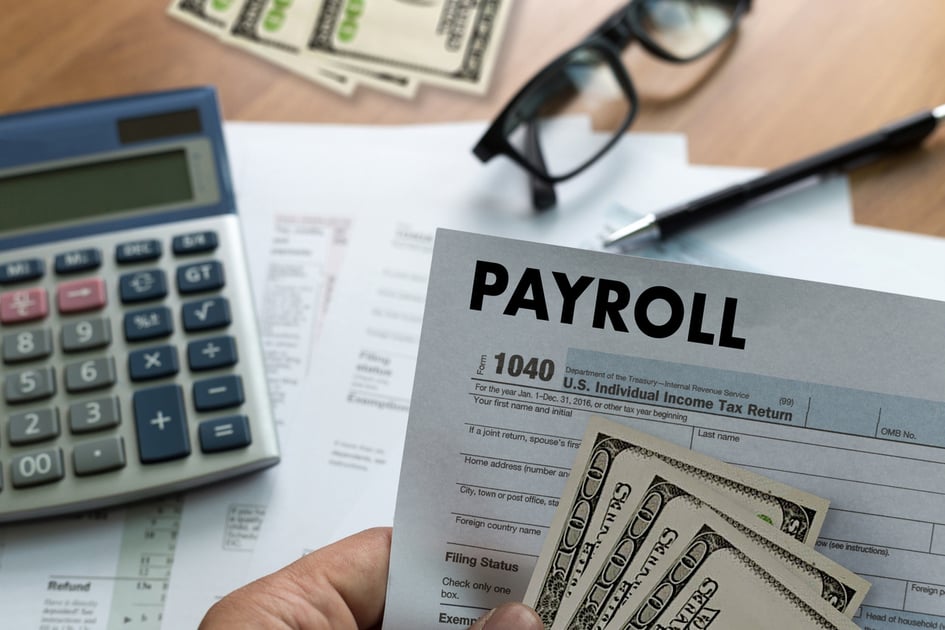 Close-up image of payroll documents, US dollar bills, and tax forms on a desk, alongside a calculator, glasses, and a pen—representing payroll processing, employee wages, and financial management.